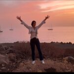 Diana Debreczeni celebrating life at sunset by the ocean, arms raised in joy and gratitude