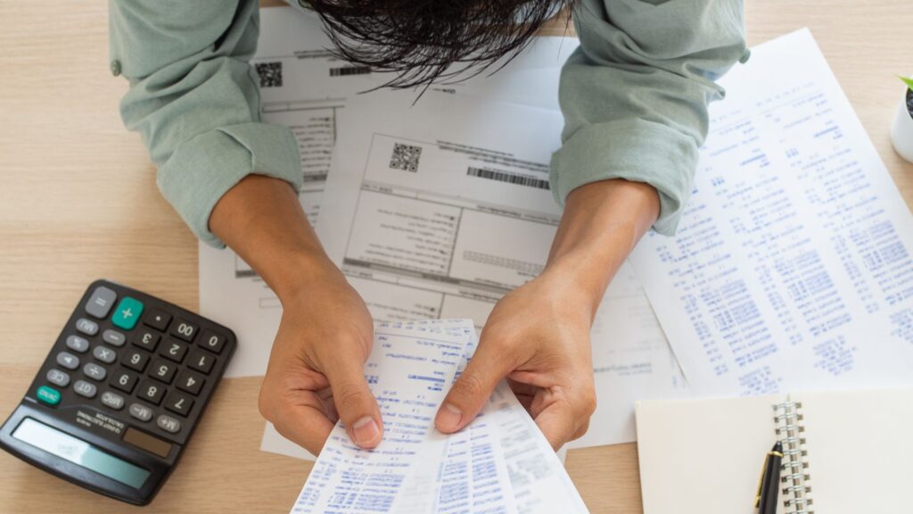 Hands reviewing receipts and bills with a calculator, illustrating financial harmony tips through budgeting and expense review.