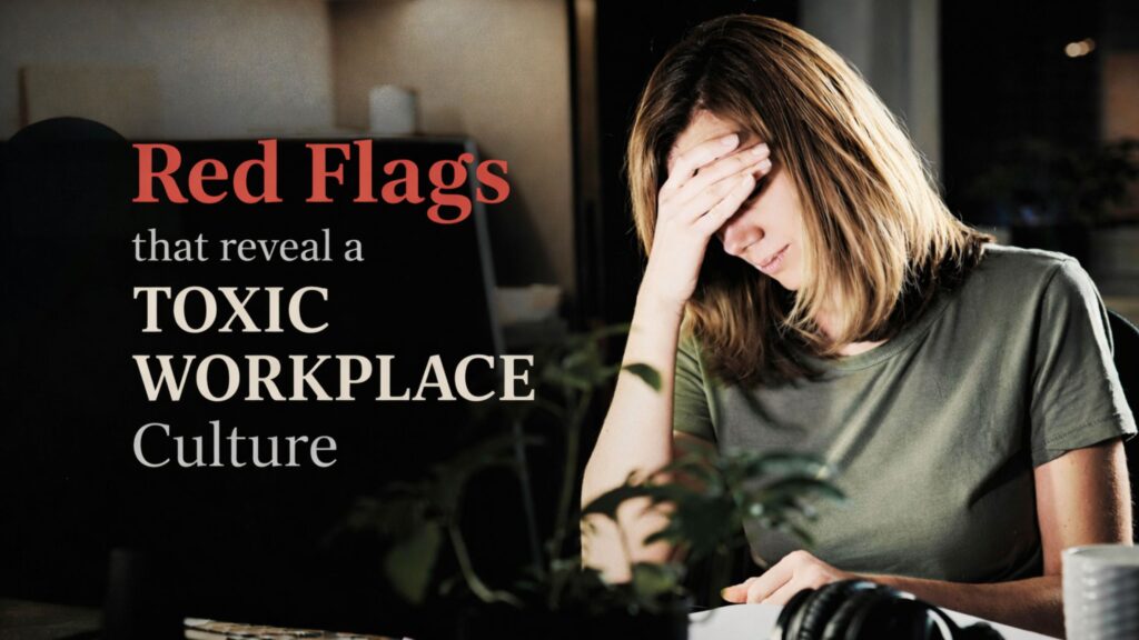 A tired woman sitting at her desk with her head in her hand, symbolizing the stress and burnout caused by a toxic workplace culture.